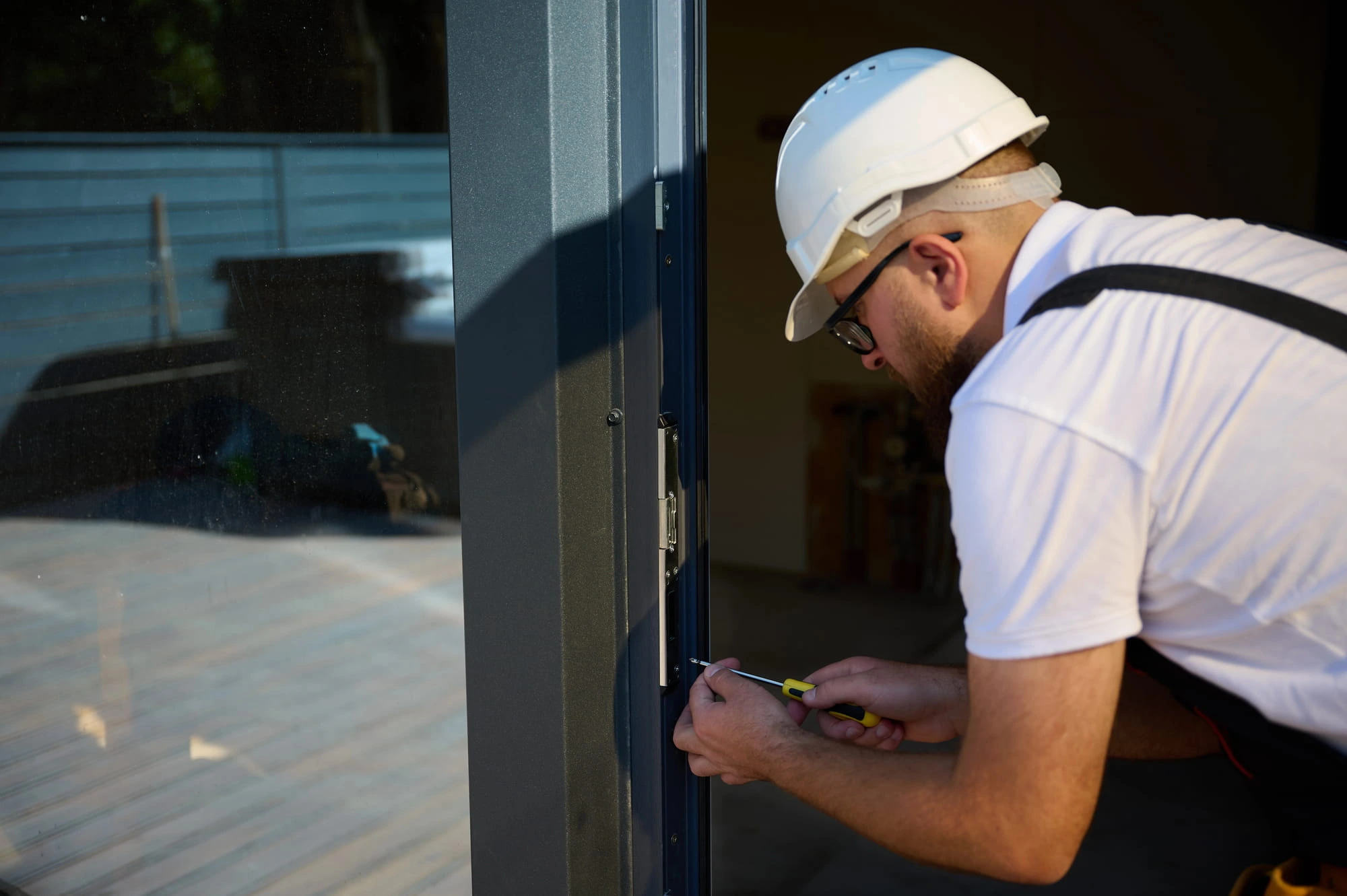 Close-up of a door frame hinge and strike being re-secured with a screwdriver on a commercial opening